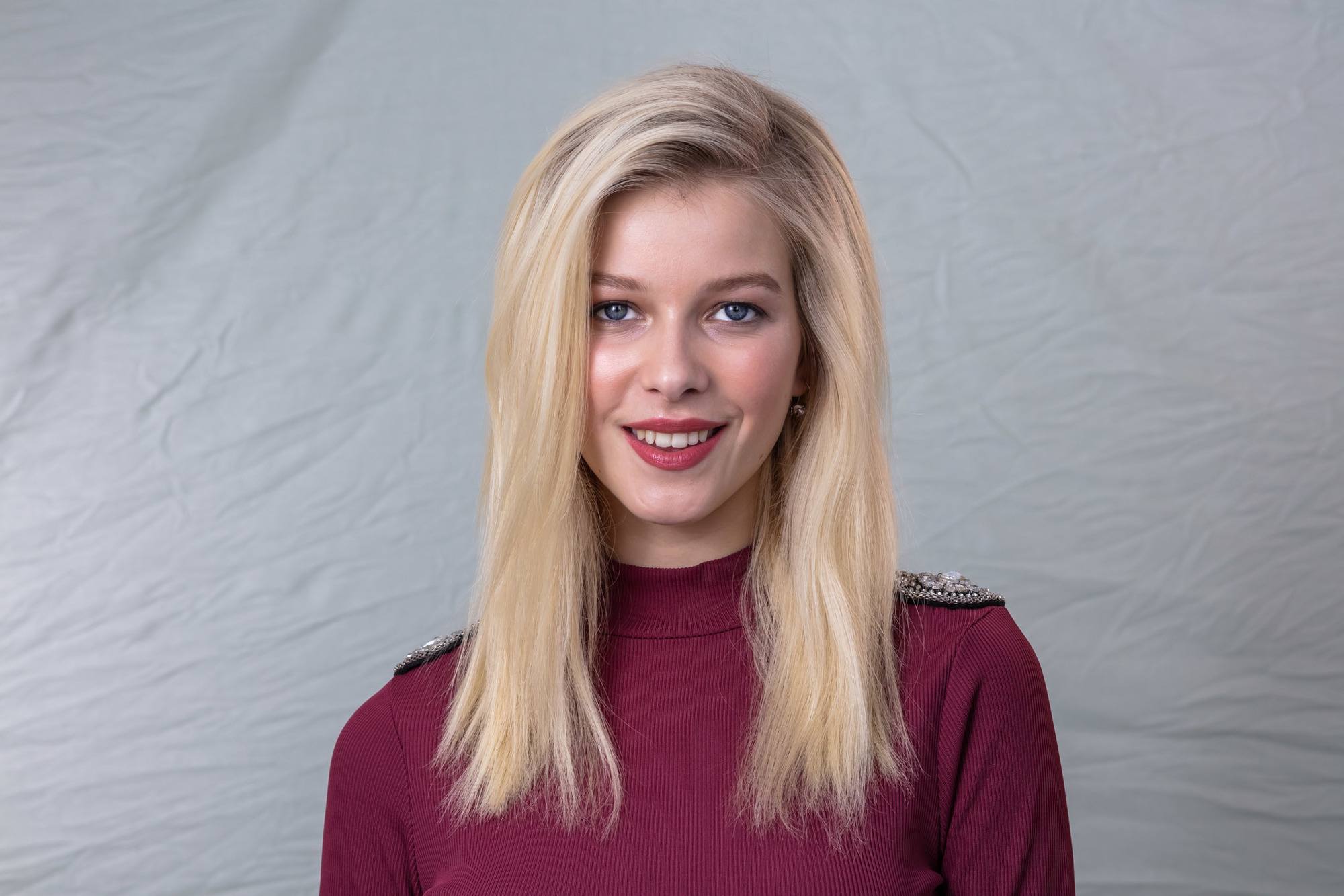 Volume hair: Landscape shot of a blonde model with straight mid-length hair, parted in a side parting, wearing a maroon high neck top