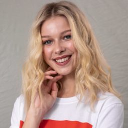 Volume hair: Blonde model with wavy tousled hair, wearing a white t-shirt with red design, touching her face with her hand