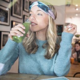 Food for healthy hair: Young blonde woman drinking vegetable juice at cafe window seat