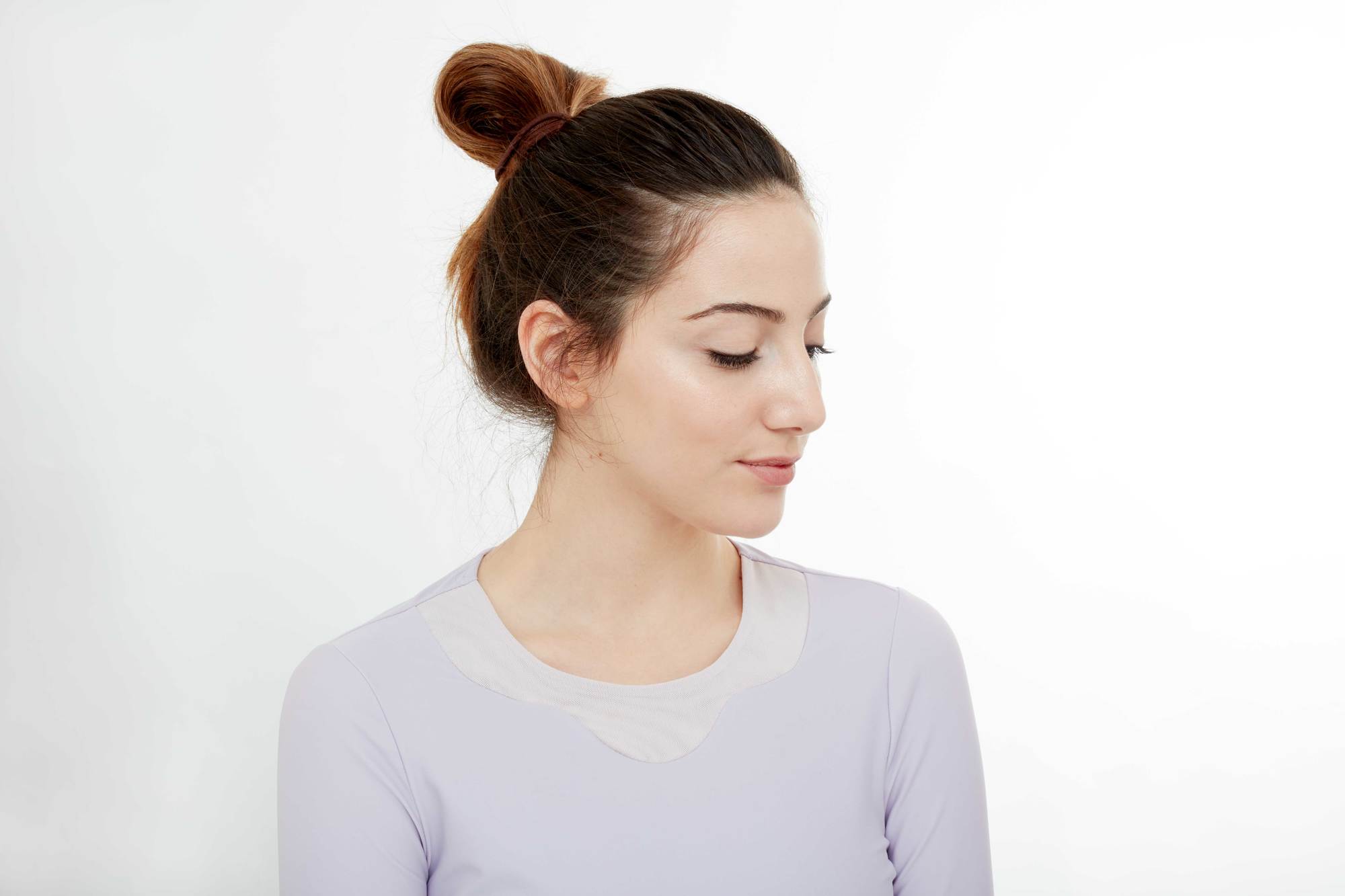 Gym hairstyles for thick hair: Brunette model with long hair tied in a looped bun, wearing a lilac gym top