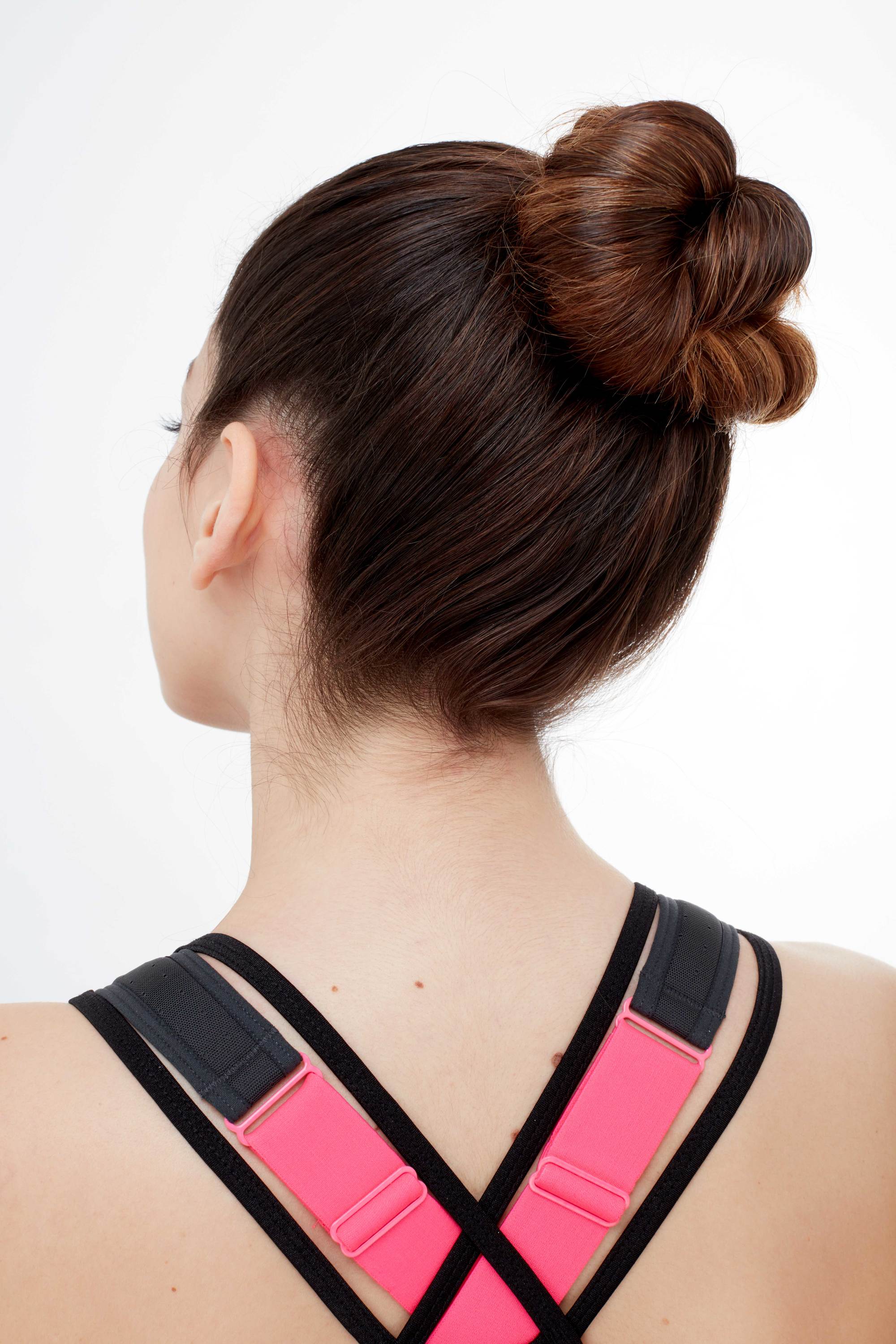 Gym hairstyles for thick hair: Back shot of a brunette model with a twisted high bun, wearing a sporty strappy top and sports bra