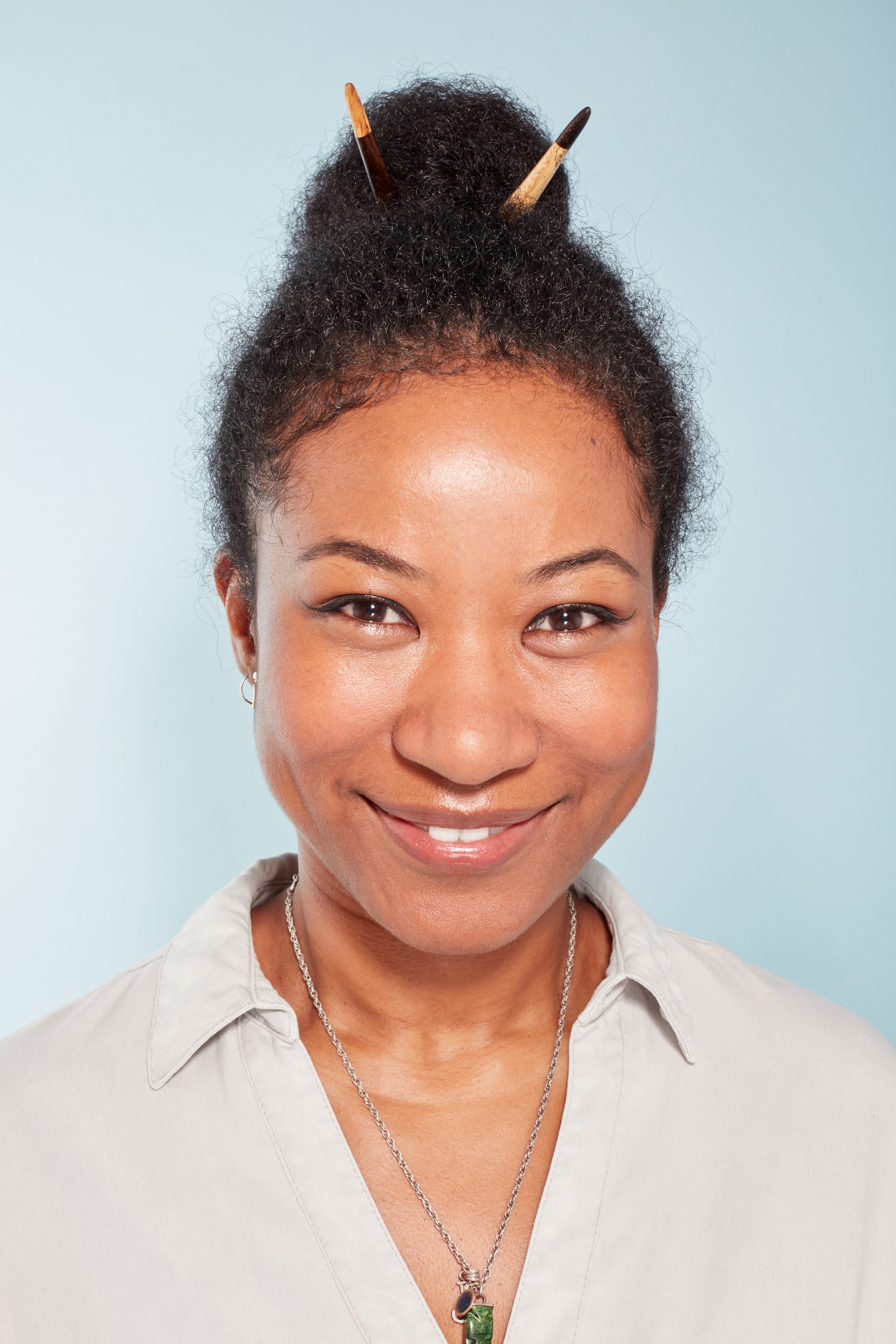 2019 accessories: All Things Hair CCO Jeanette with her hair in a bun with wooden chopstick hair accessories, wearing a neutral shirt