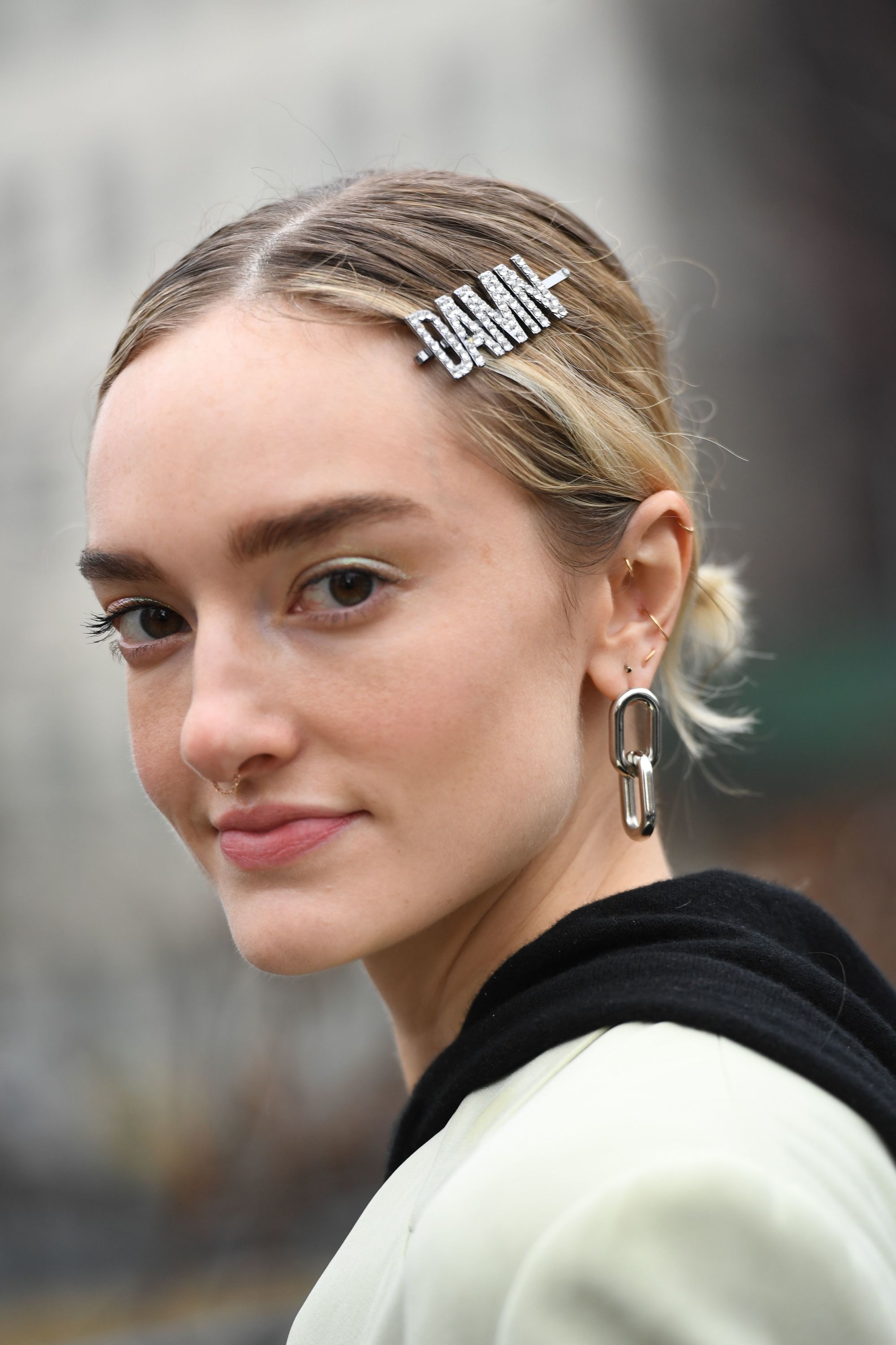 2019 hair accessories: Close-up street style photo of a blonde woman with her hair in a low bun wearing a diamante slogan 'damn' hair clip.