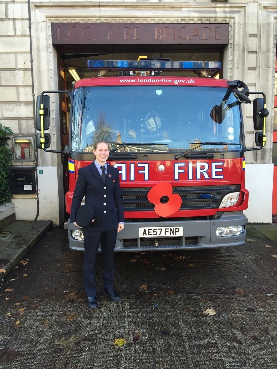 Working It: Woman with blonde hair in a bun updo standing in front of afire engine.