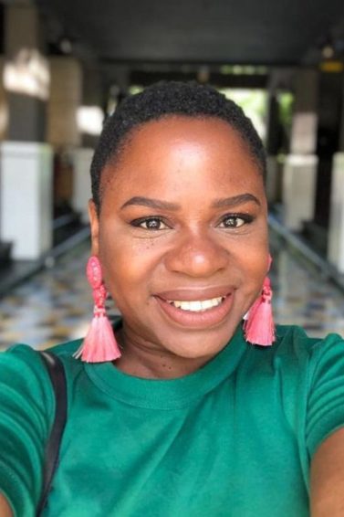 Real Hair Stories Nadia Williams: Young black woman with shaved hairstyles wearing a green top and statement earrings