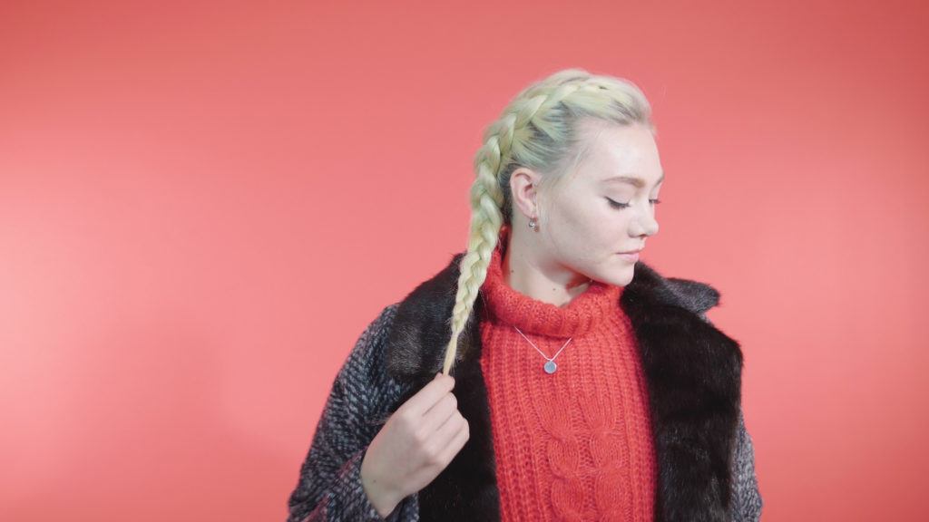 Side Dutch braid tutorial: Blonde girl with a side Dutch braid, wearing a red knit jumper and a coat