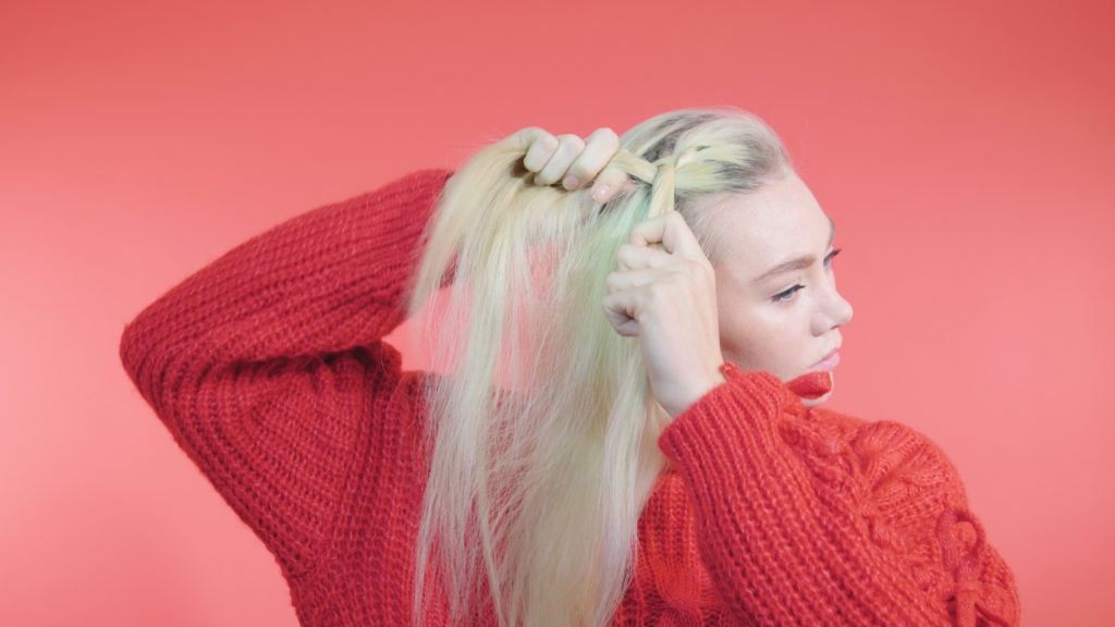 Side Dutch braid tutorial: Blonde with long straight hair braiding her fringe, wearing a red knit jumper