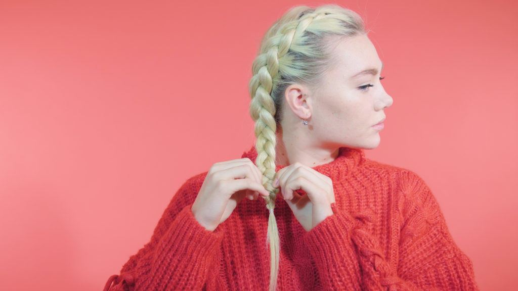Side Dutch braid tutorial: Blonde girl with a side Dutch braid pancaking her braid, wearing a red knit jumper