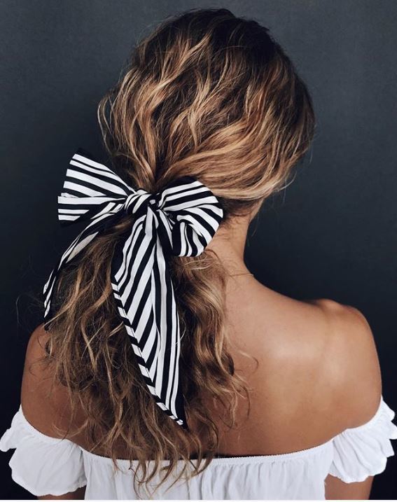 Woman with curly dirty blonde long hair in ponytail with striped bow