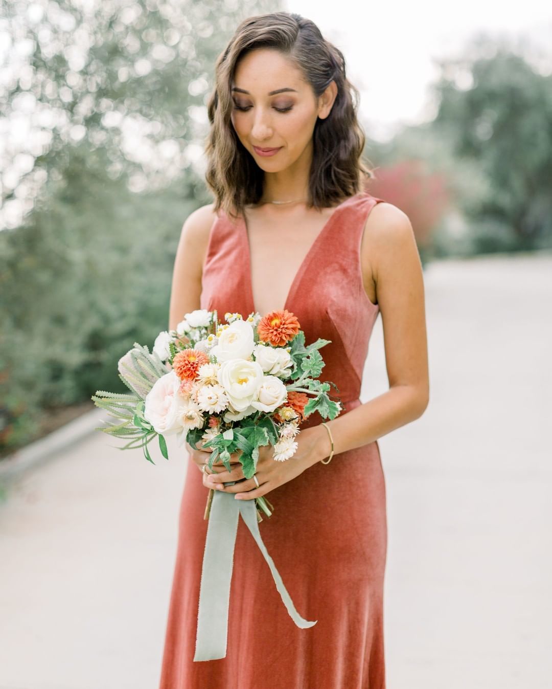 Bridesmaid hairstyles: Woman with short brown hair swept to the side with loose waves, wearing bridesmaid dress and posing for picture