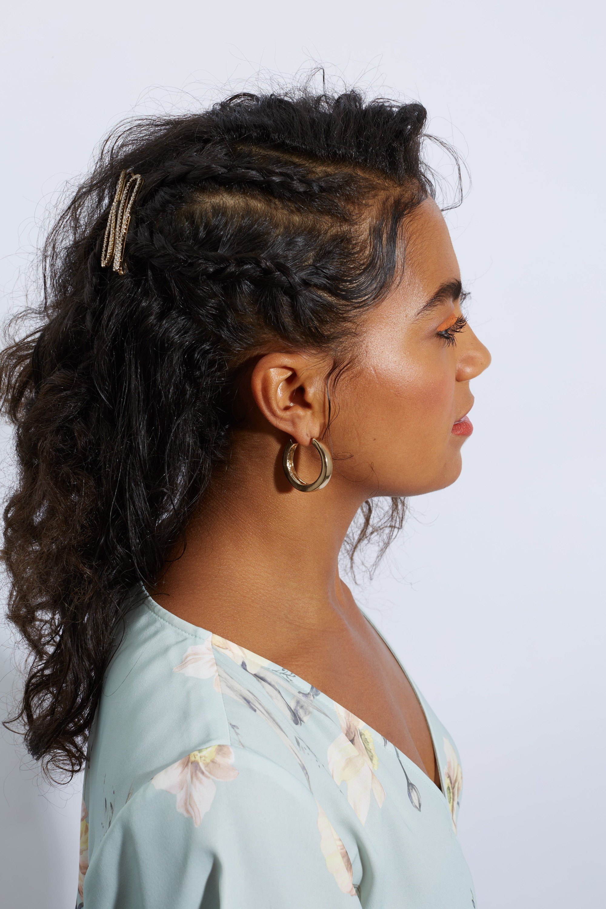 Bridesmaid hairstyles: Woman with loose naturally curly hair styled into half side braids with clips, wearing hoops and floral dress