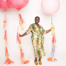 A black woman happily laughing while holding pastel pink balloons