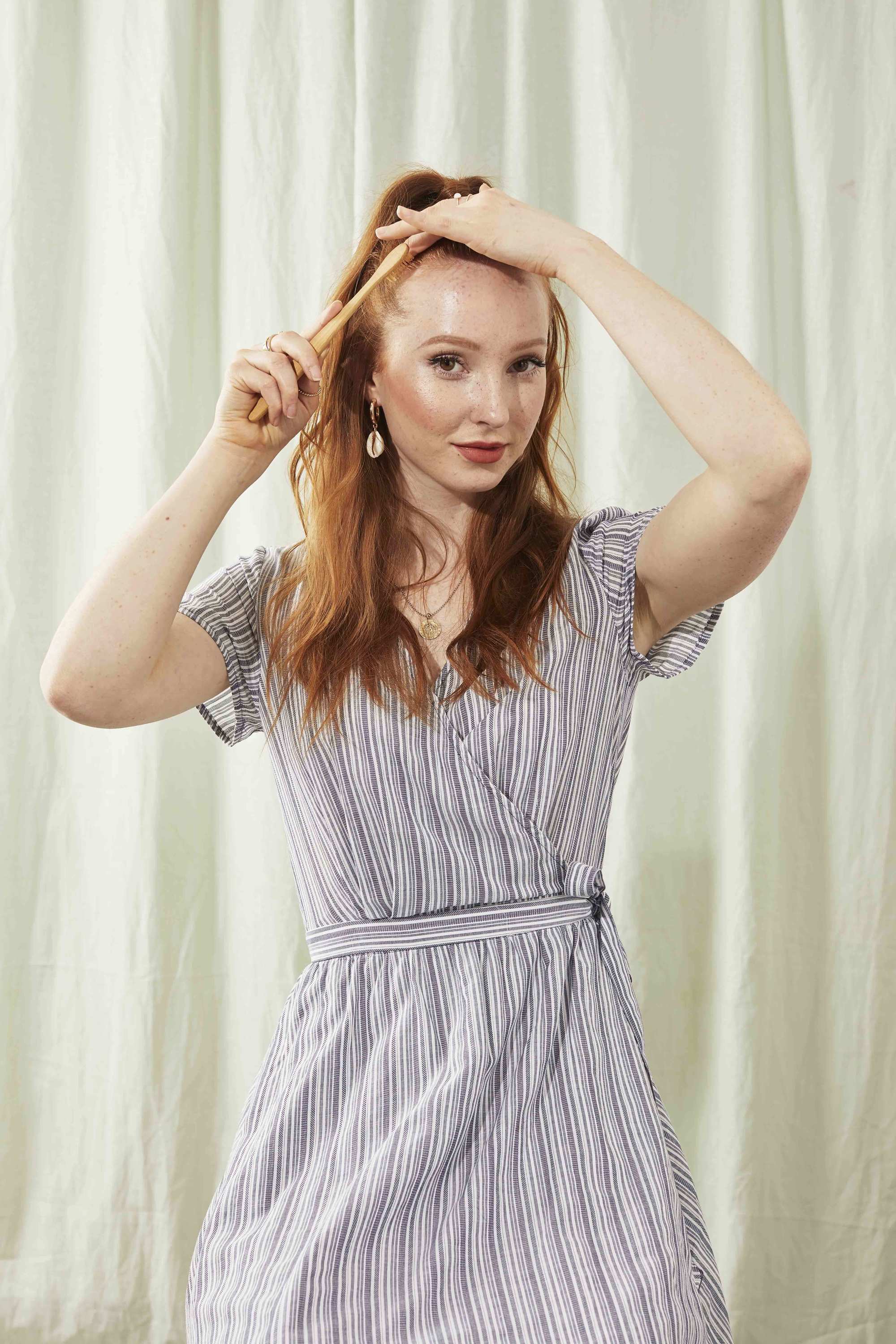 Redhead woman using a toothbrush to smooth her hair