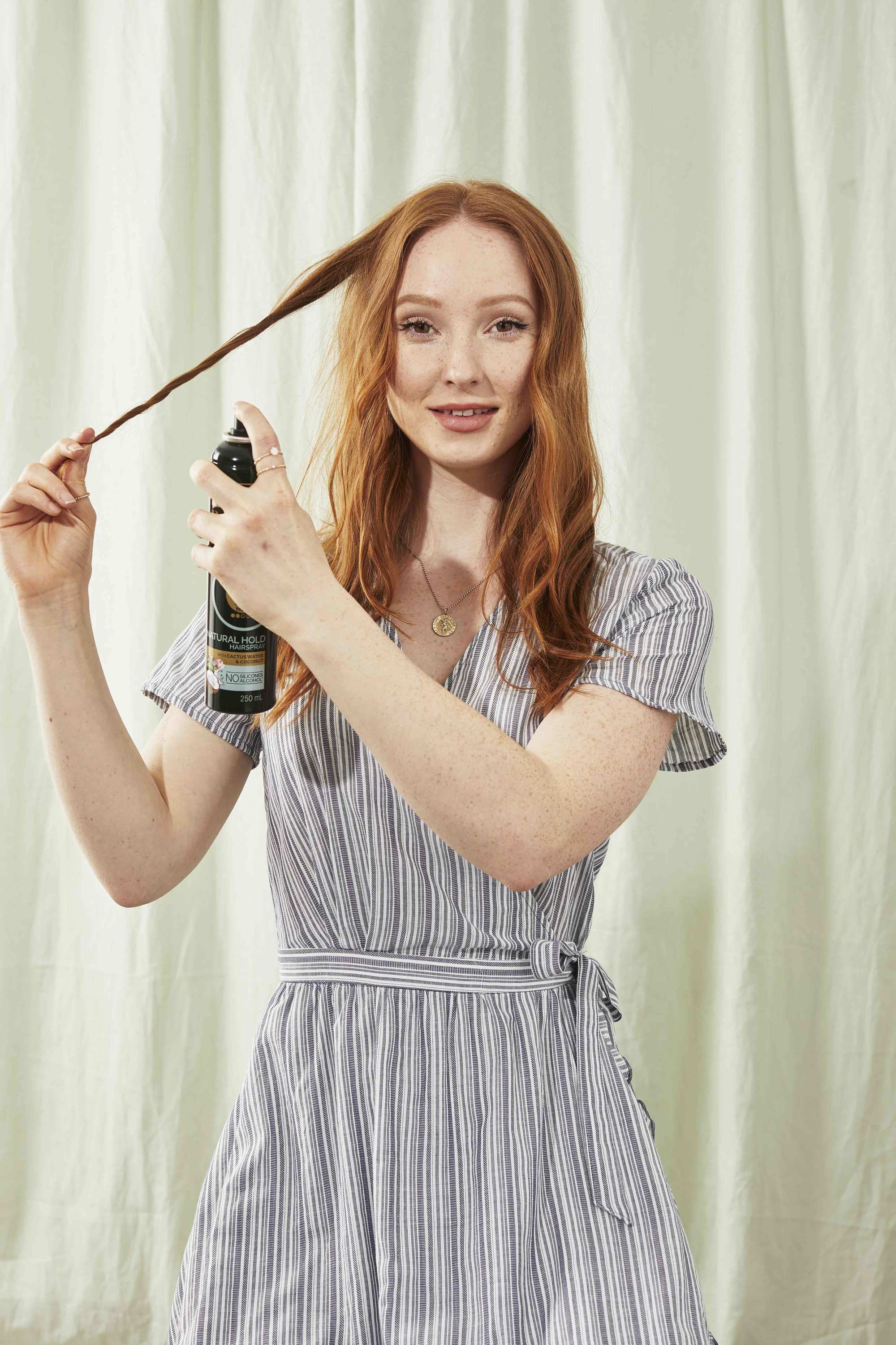 Redhead woman twisting a section of hair and spraying with hairspray
