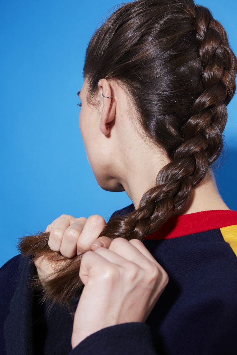 Brunette woman braiding her hair in a Dutch braid