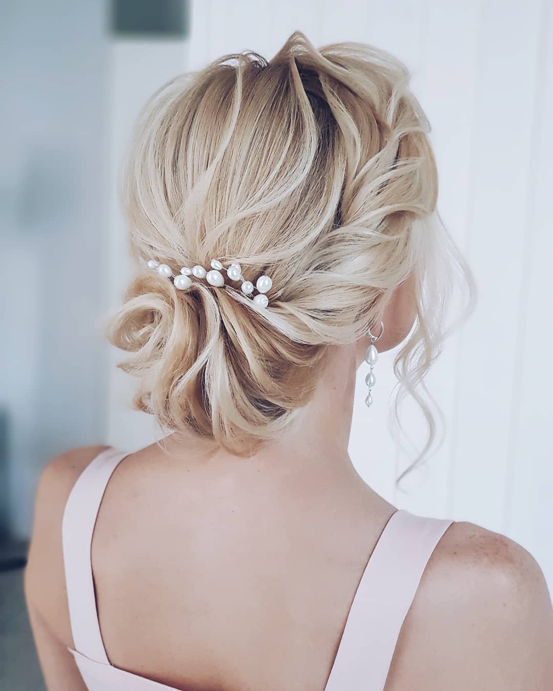 Woman with blonde hair styled into a romantic low wavy bun with pearl pins