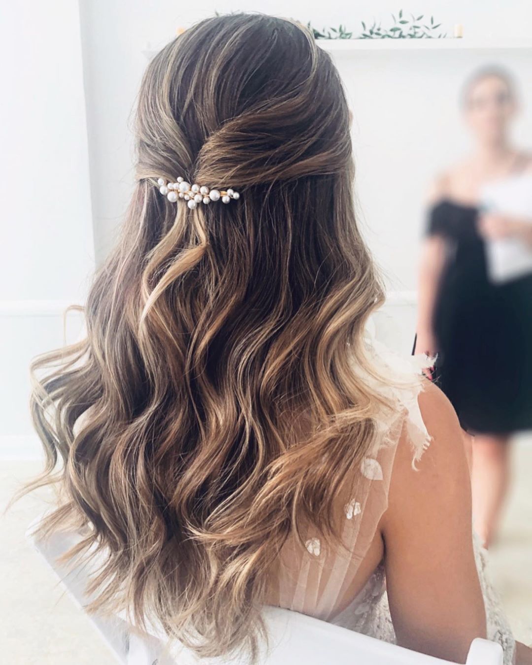Woman with half-up, half-down wavy brown hair with pearl hair pin