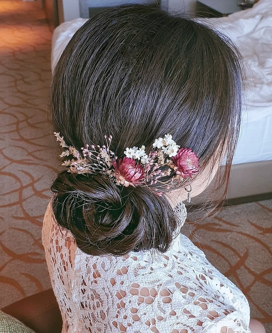 Woman with dark brown hair styled into a low textured side bun with flowers
