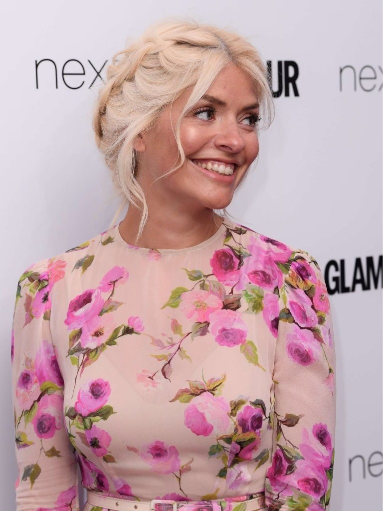 Holly Willoughby hair gallery: Holly Willoughby with light blonde hair in double dutch braids with loose tendrils wearing a light pink floral long sleeve dress.