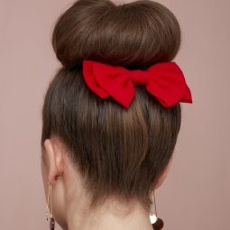 Woman with dark hair styled into a bun with red hair bow