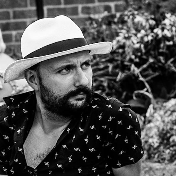 Black and white image of a bearded man wearing a white hat