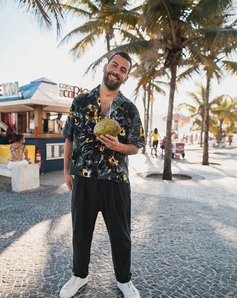 matthewzorpas: bearded man wearing a tropical shirt and holding a coconut on the beach