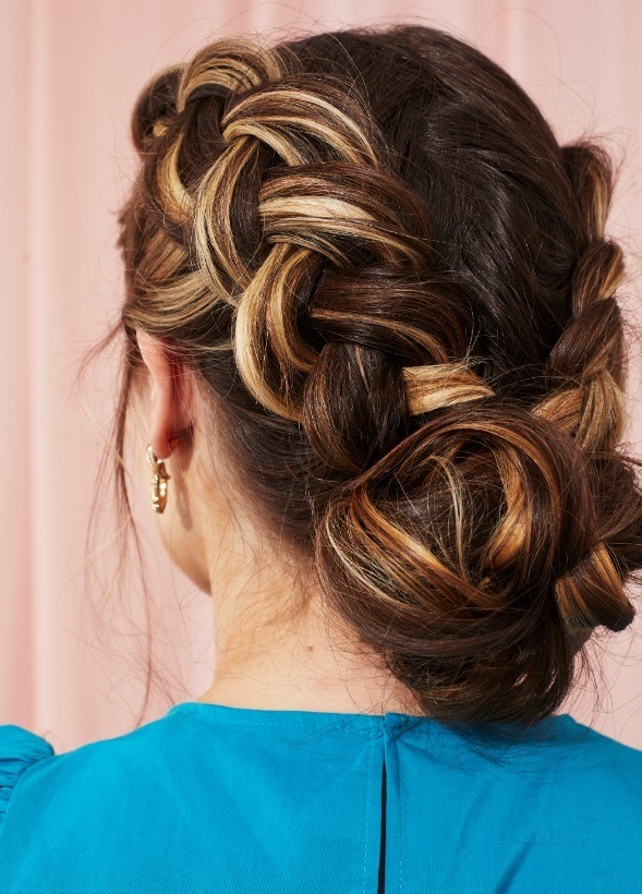 Woman with brunette and blonde highlighted hair in a double Dutch braided bun hairstyle