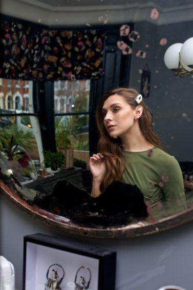 Woman with long brown wavy hair with pearl hairclip looking int he mirror