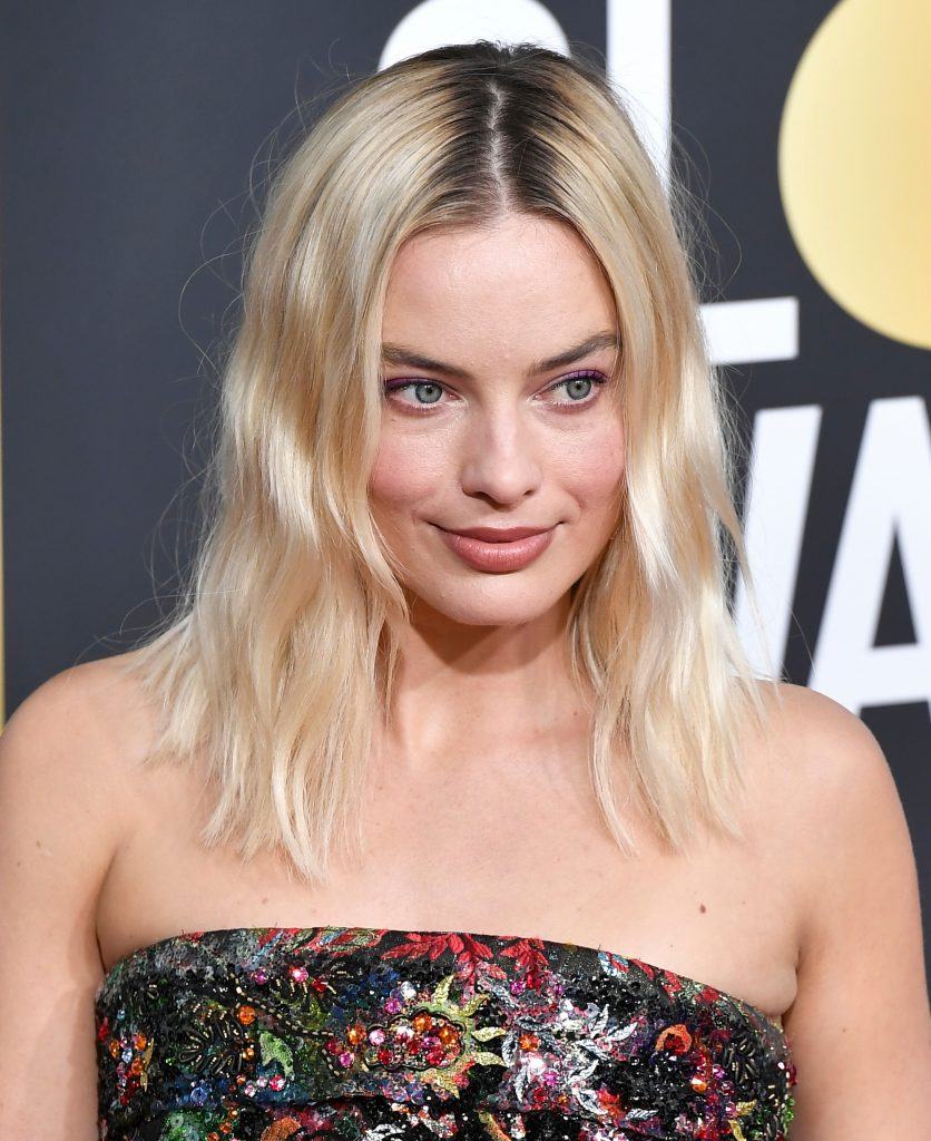 Margot Robbie with wavy blonde mid-length hair with dark roots