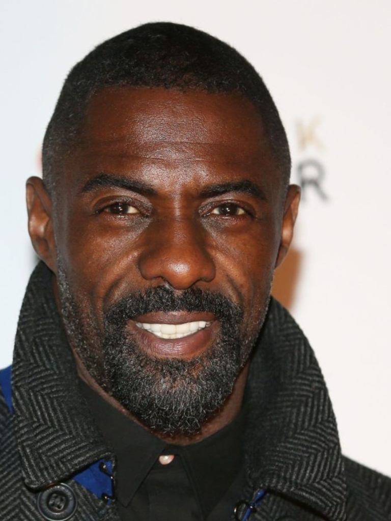 Idris Elba wearing a black shirt with a buzz cut and a beard.