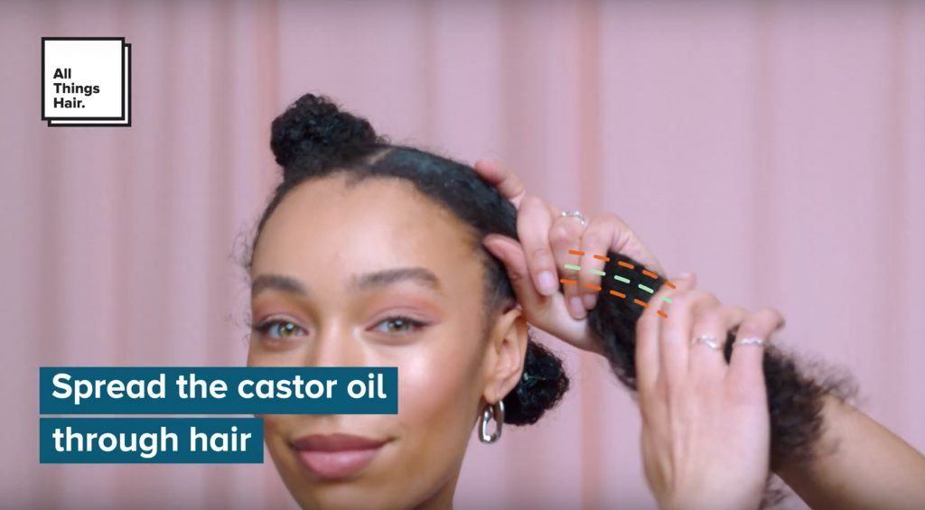 Natural haired woman smoothing castor oil through a section of hair