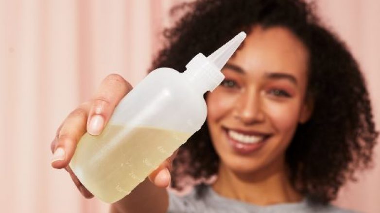 Woman with naturally curly short hair holding a bottle of oil