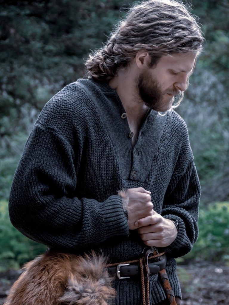 Man with brown curly hair in a low man bun