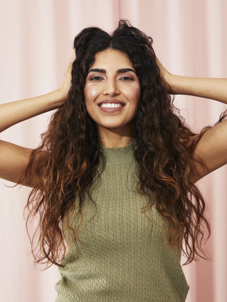 Woman with dark brown curly hair touching it with her hands.