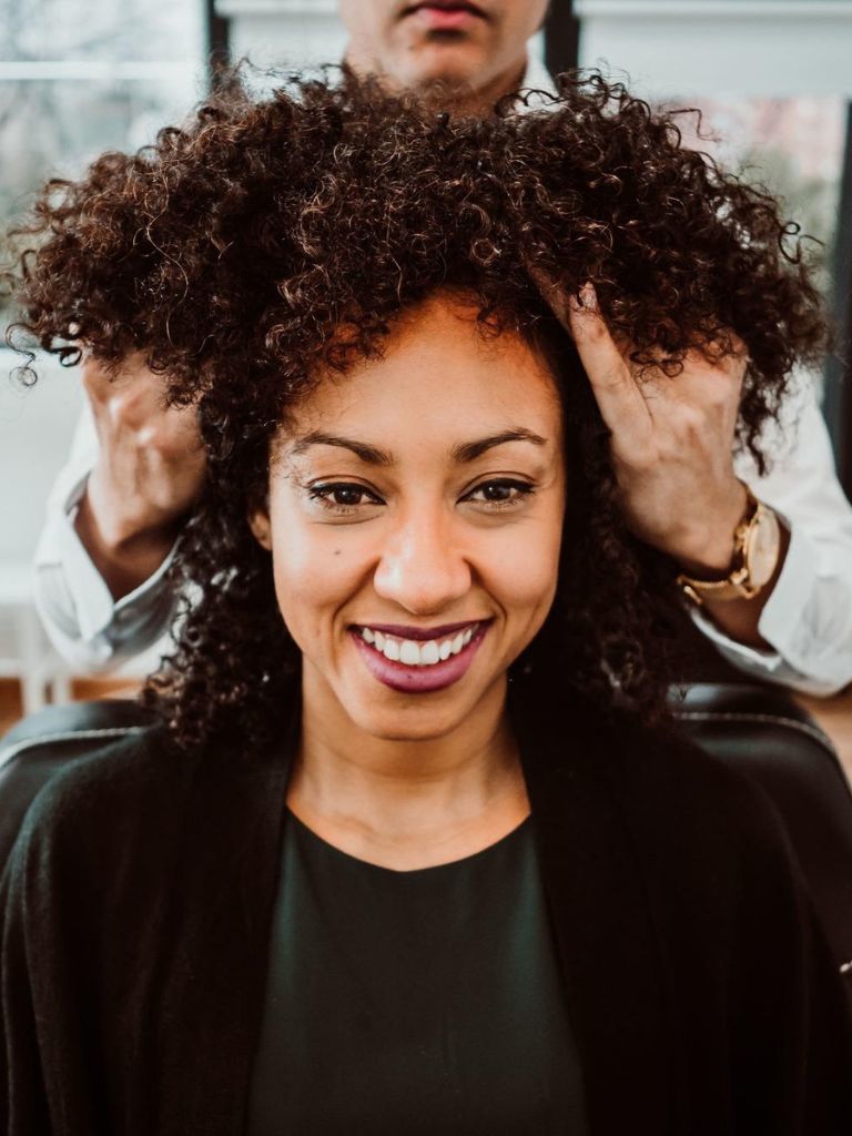 Woman with tight curls smiling in a hair salon getting a keratin hair treatment for curly hair.