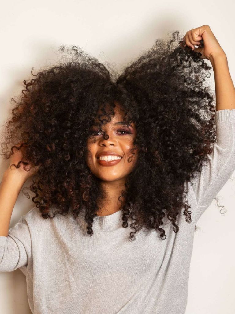 Woman with natural curly afro hair touching it with her hands.