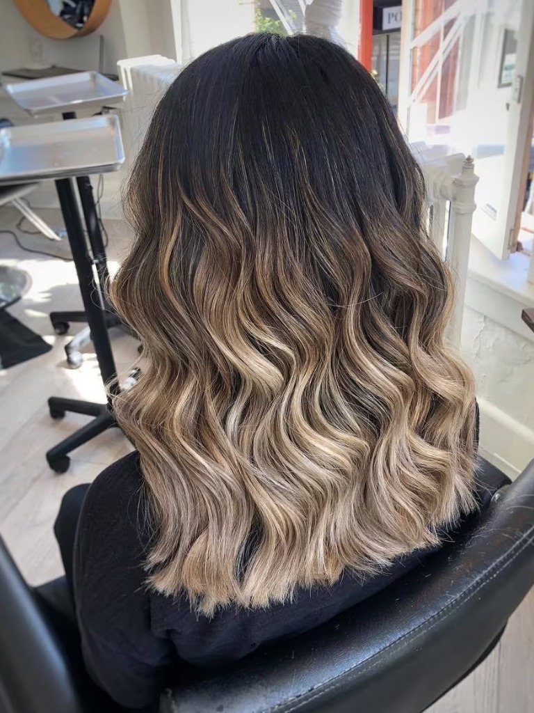 Woman with mid-length curly black to blonde balayage hair