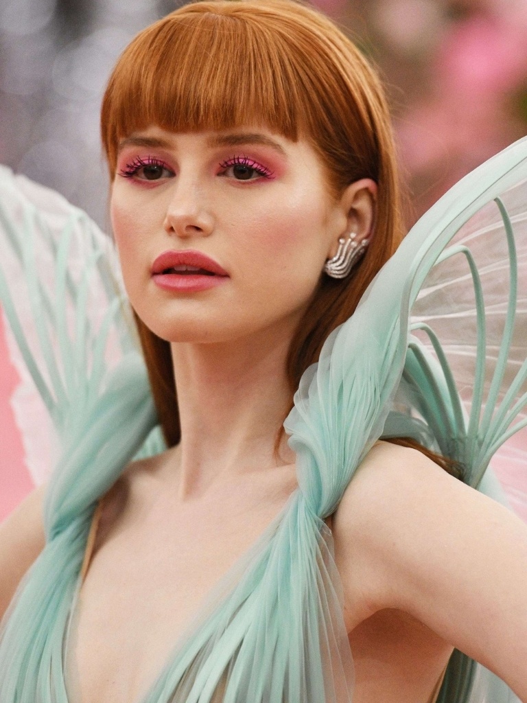 Famous redheads: Madelaine Petsch with long straight bright copper hair with full micro fringe wearing a light green dress with statement shoulder detail.