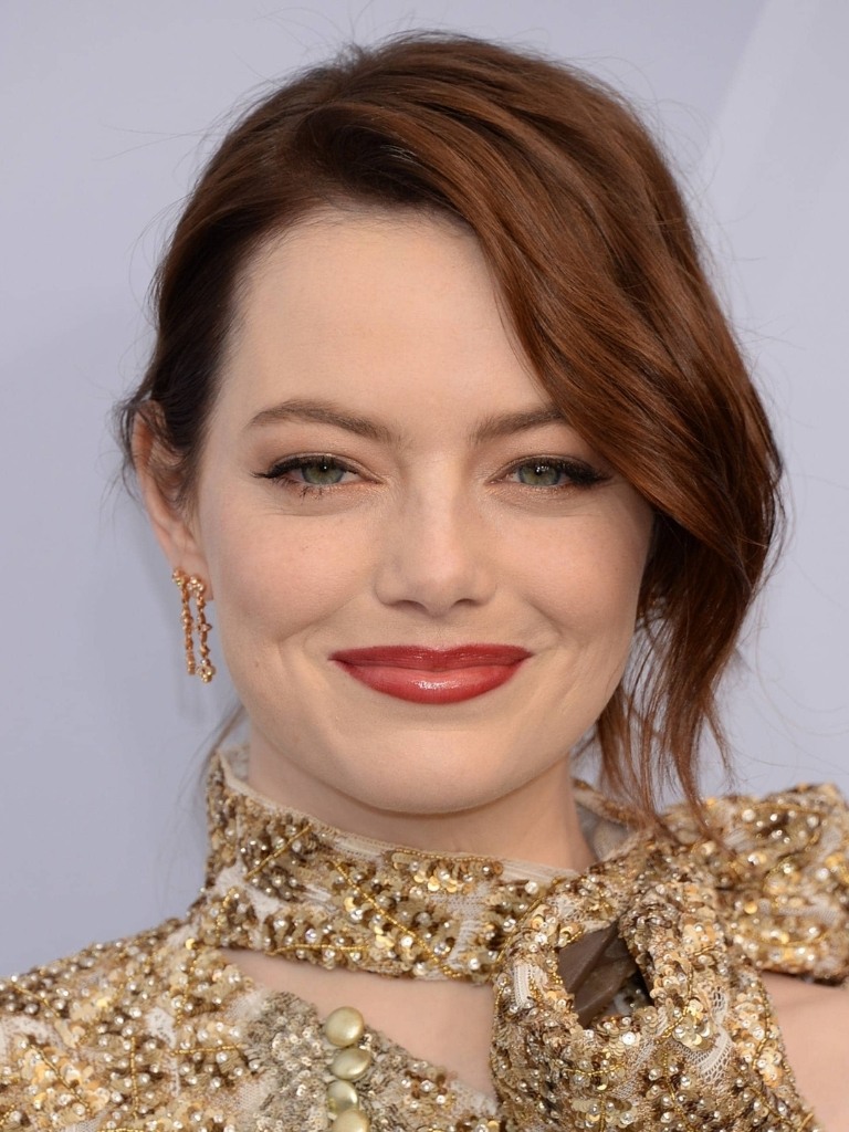 Famous redheads: Emma Stone with dark red wavy hair styled in a updo with a loose long side fringe wearing a gold high neck dress.