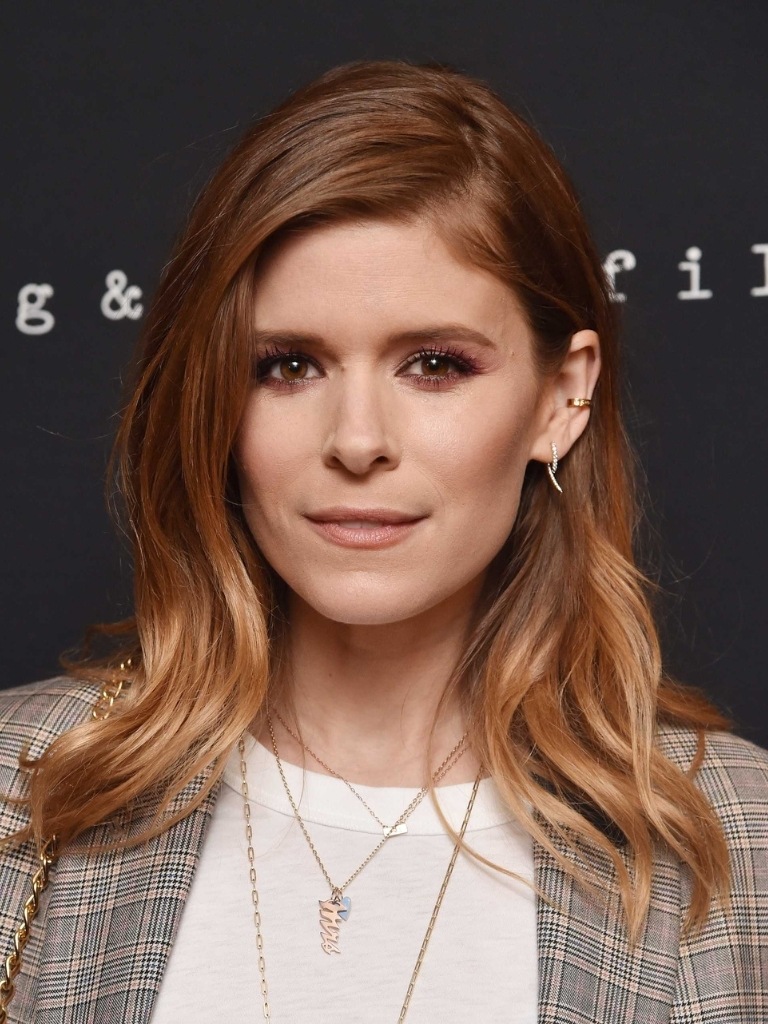 Famous redheads: Kate Mara with medium length wavy auburn red brown balayage wearing a white t shirt and grey checked blazer.