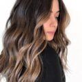 Woman with long wavy brunette hair with face framing balayage