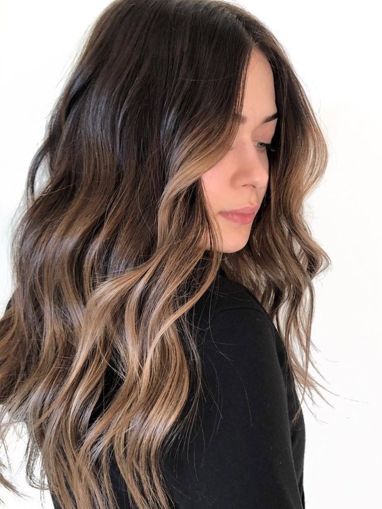 Woman with long wavy brunette hair with face framing balayage