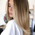 Woman with blown out, long light brown hair with golden balayage hair colour