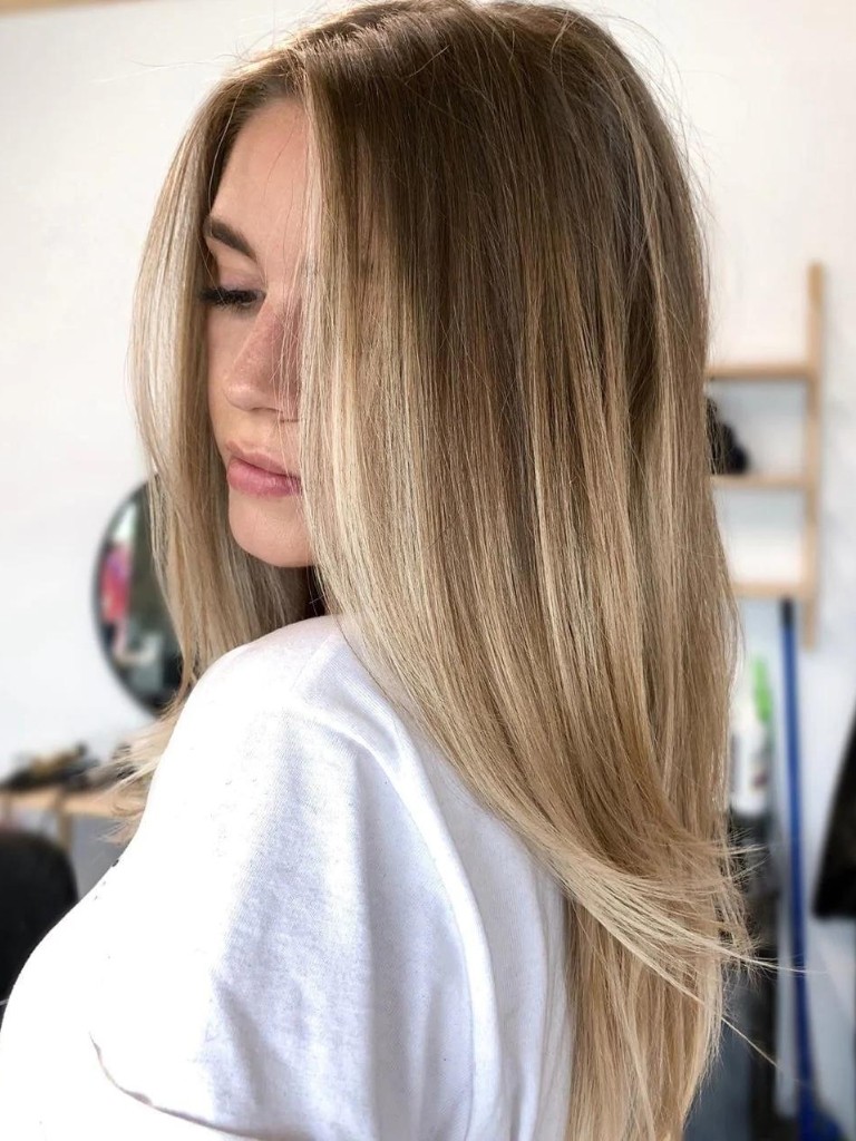 Woman with blown out, long light brown hair with golden balayage hair colour