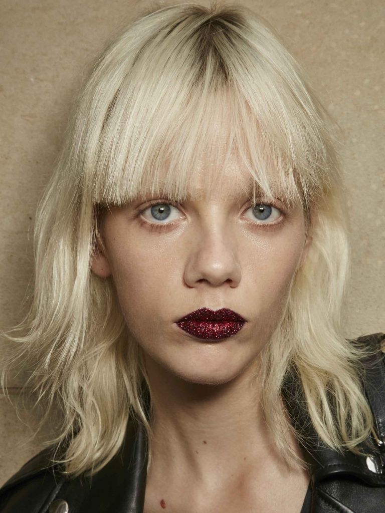 model with platinum blonde hair cut into a short shag haircut and blunt bangs, wearing dark red lipstick