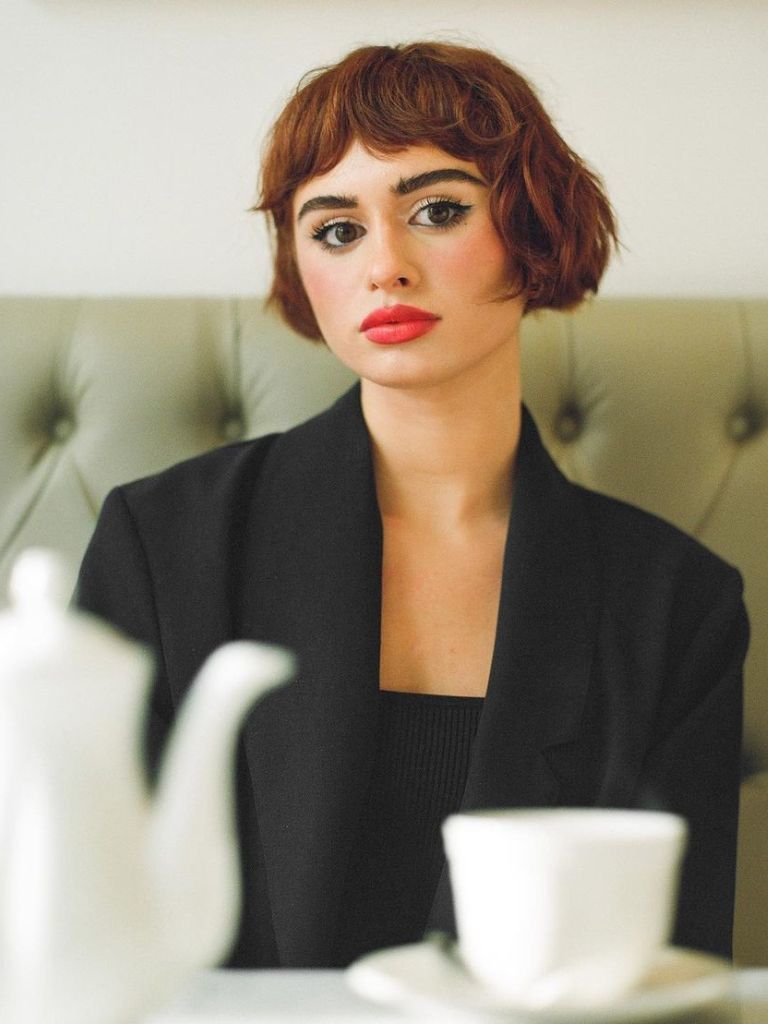 Woman with a red French bob and red lipstick sitting in a cafe.