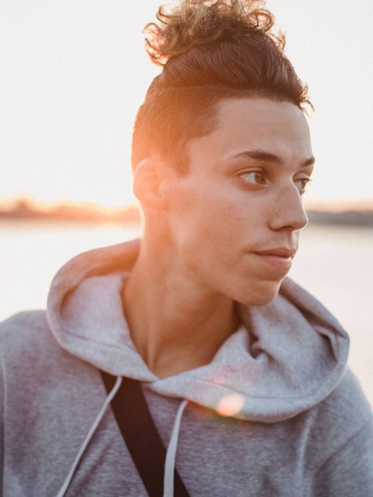 Man looking to side wearing a curly topknot hairstyle with extreme fade. Soft light at sunset