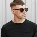 Man with short cut with tapered fade undercut hairstyle and short fringe with pointed middle. He wears sunglasses and a black t-shirt