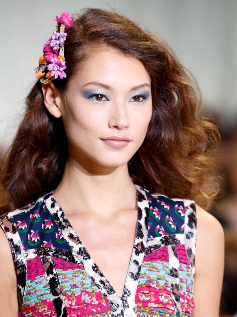 Asian hairstyles: Asian woman with golden caramel brown curly hair with floral hair accessory wearing a patterned dress.