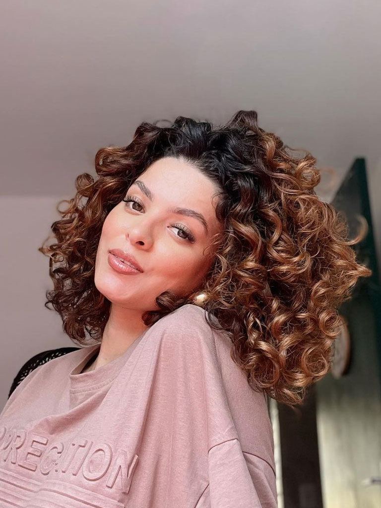 Hispanic woman with thick loose curled hairstyle dark roots and copper lengths looking to camera